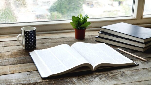 Open book on a study table beside a stack of books